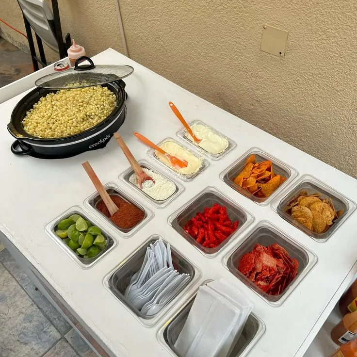 Esquites table with toppings, chips and lime from Delicias Factory catering