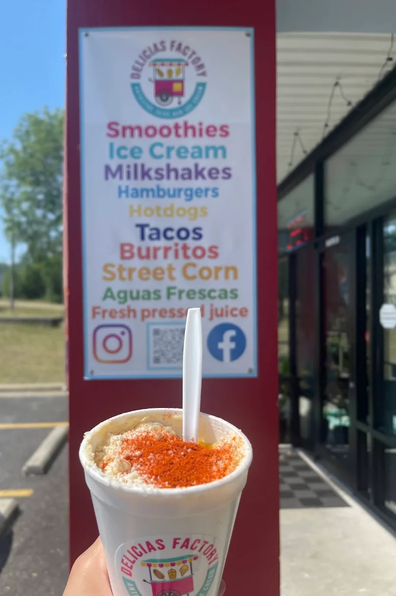 Elote en vaso in front of the original Delicias Factory sign on the 76 Strip in Branson